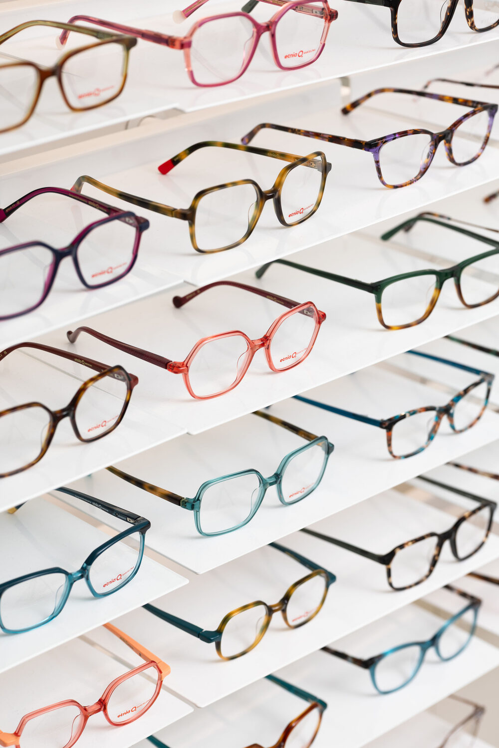 Rows of colourful designer spectacle frames on a display wall at Auerbach and Steele opticians, King's Road Chelsea, London retail product photography